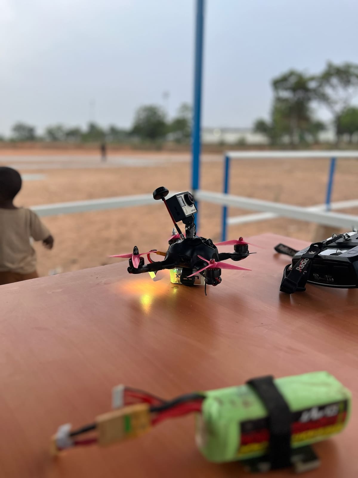 FPV racing quadcopter fitted with an action camera, beside its radio and battery